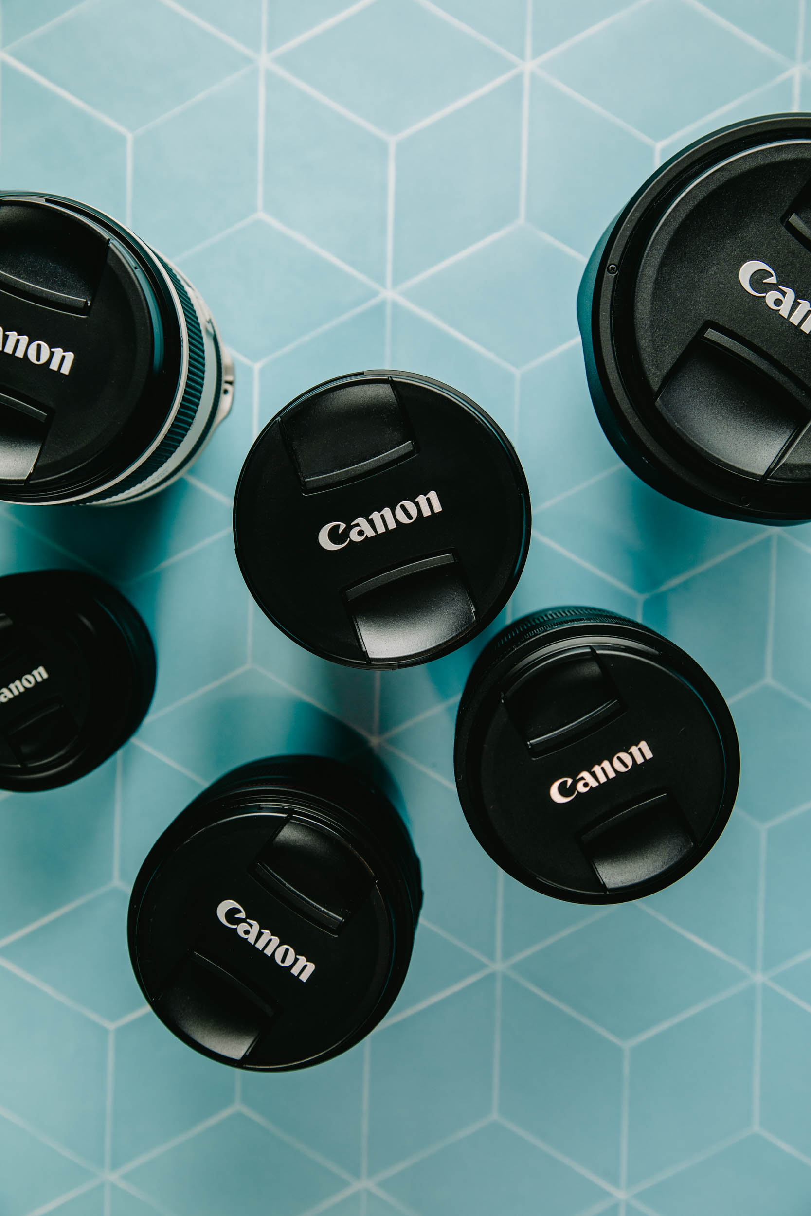 overhead view of six Canon lenses on a teal surface, including the top travel lenses.